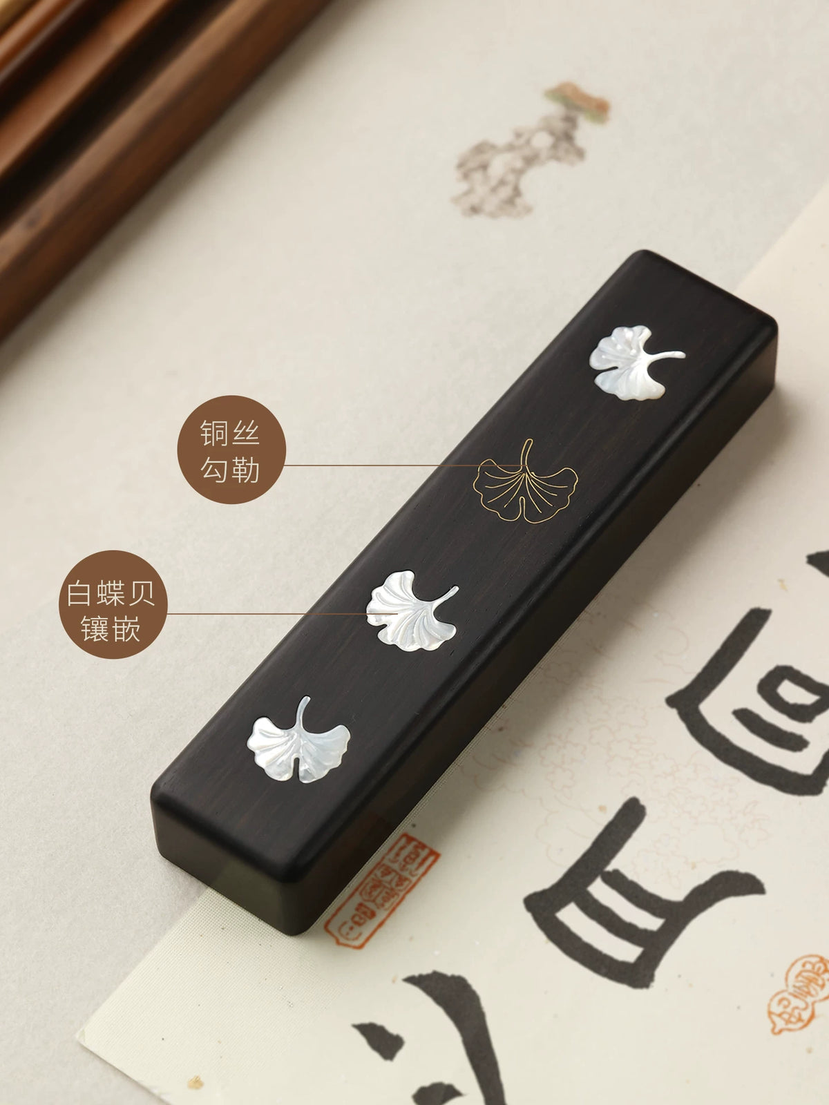 Ebony Chinese calligraphy paperweight showing white shell leaves and a brass leaf outline on calligraphy paper