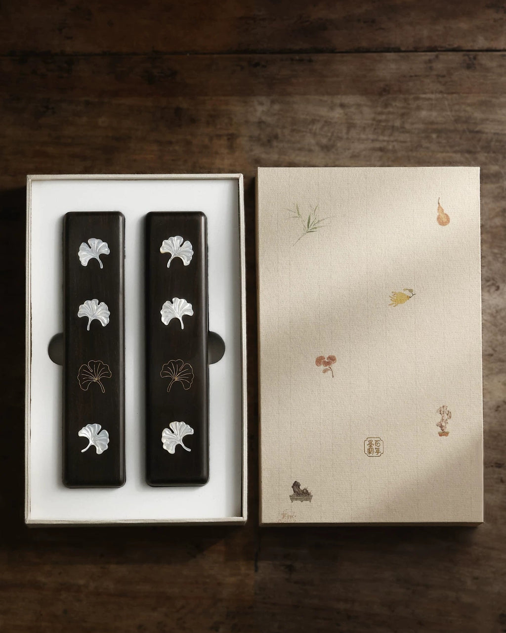 Two ebony Chinese calligraphy paperweights with ginkgo leaf inlay in an open illustrated gift box