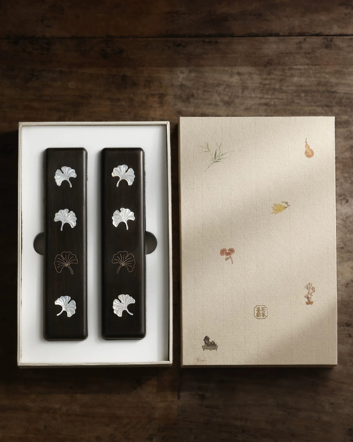 Two ebony Chinese calligraphy paperweights with ginkgo leaf inlay in an open illustrated gift box