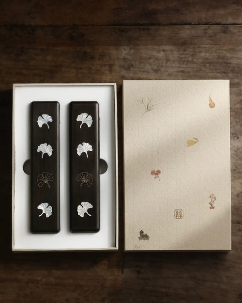 Two ebony Chinese calligraphy paperweights with ginkgo leaf inlay in an open illustrated gift box