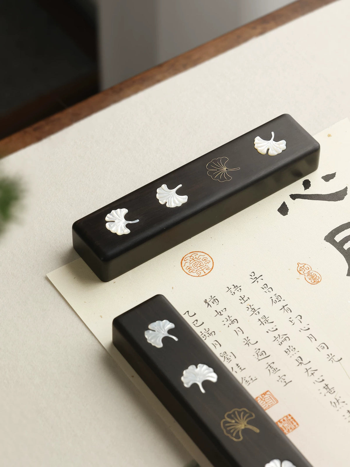 Ebony Chinese calligraphy paperweights with shell ginkgo leaf inlay resting on a brush-written artwork