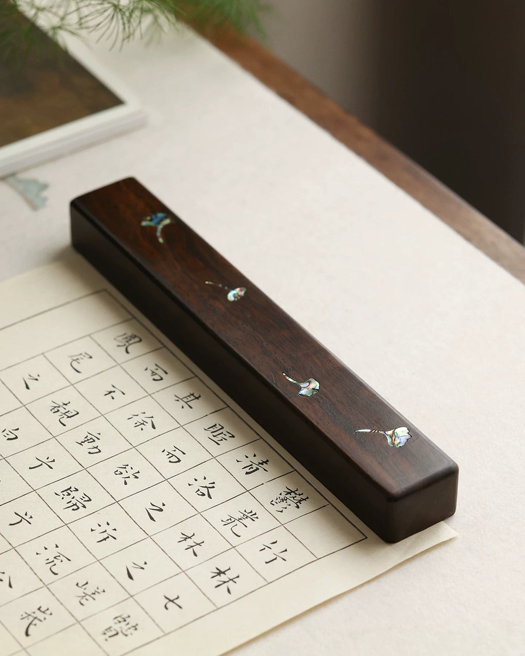Chinese calligraphy wood paperweight with mother-of-pearl ginkgo leaves on gridded practice paper