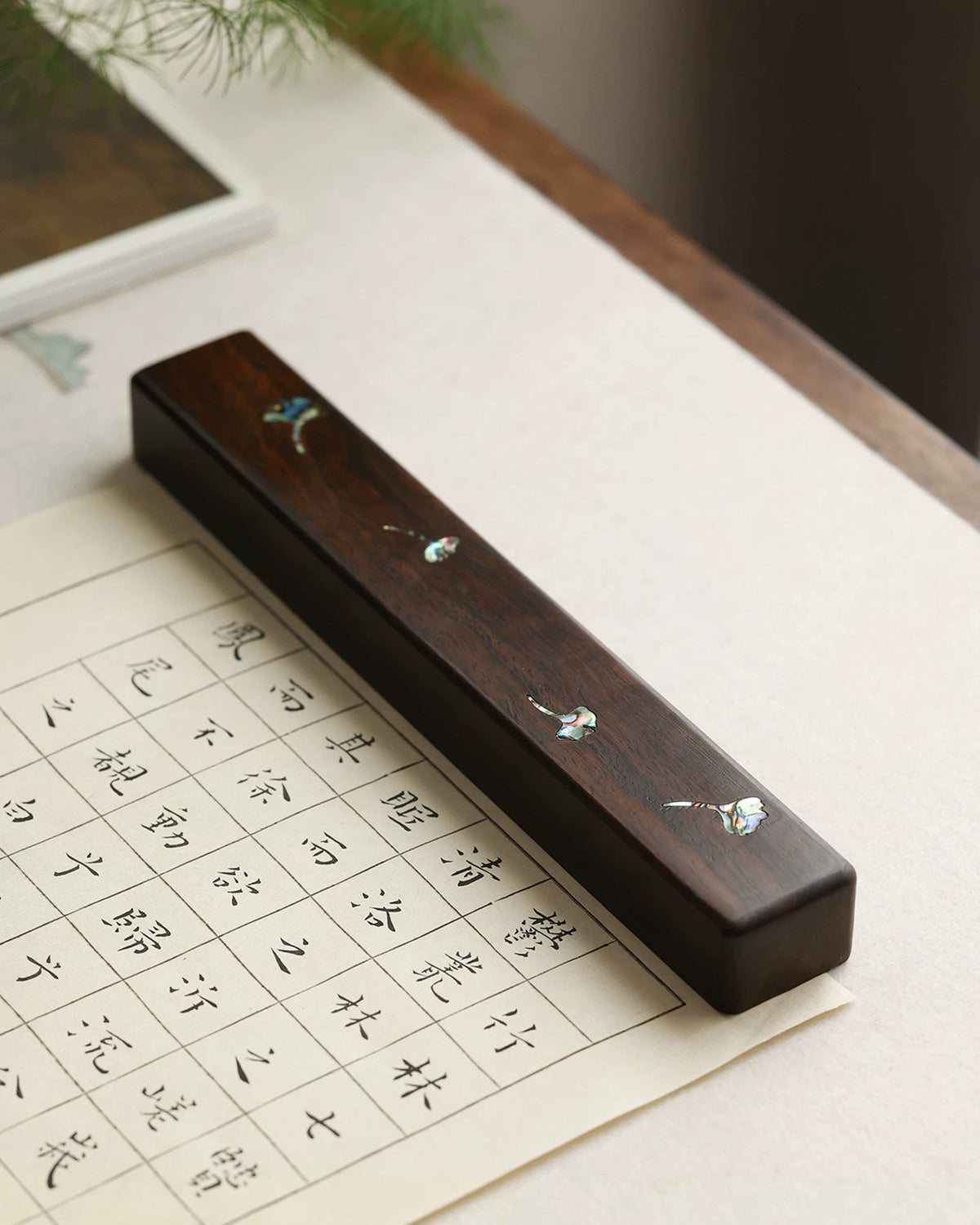 Chinese calligraphy wood paperweight with mother-of-pearl ginkgo leaves on gridded practice paper