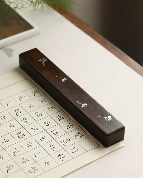 Chinese calligraphy wood paperweight with mother-of-pearl ginkgo leaves on gridded practice paper