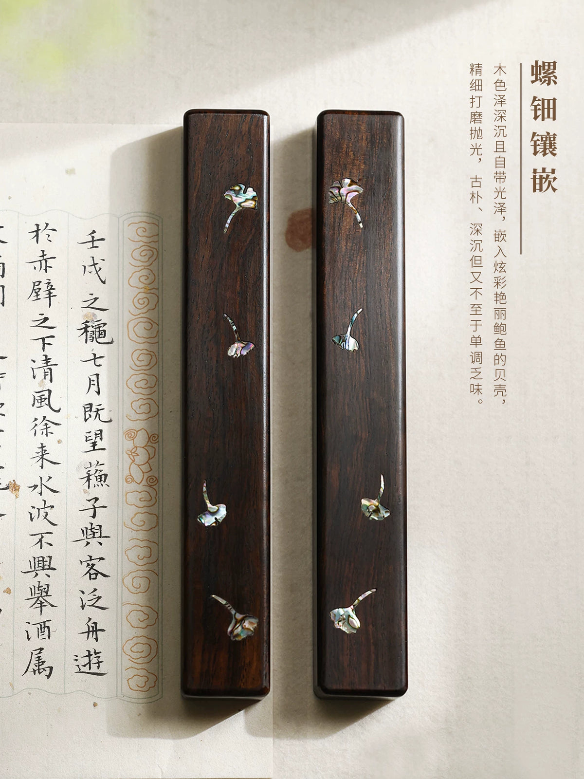 Pair of dark wooden Chinese calligraphy paperweights with iridescent shell ginkgo leaves beside calligraphy