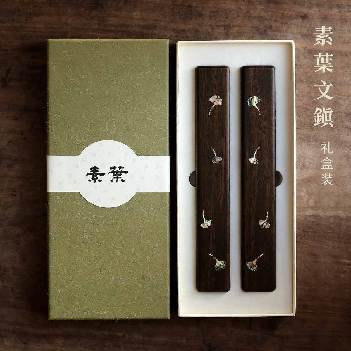 Two wooden Chinese calligraphy paperweights with shell leaf inlay in an open green gift box