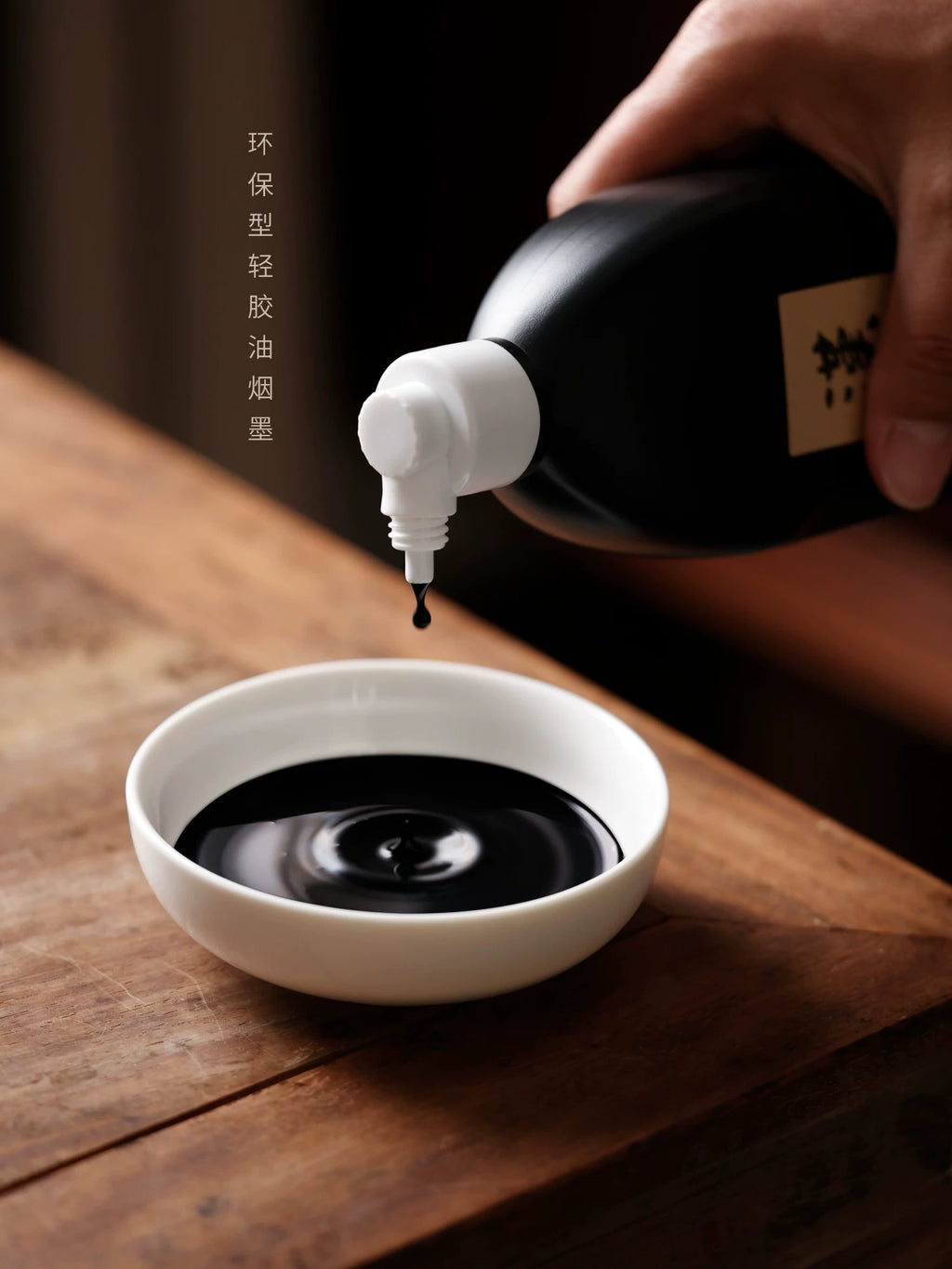 Hand pouring Hanmo black Chinese calligraphy ink from a dispensing bottle into a white ceramic dish