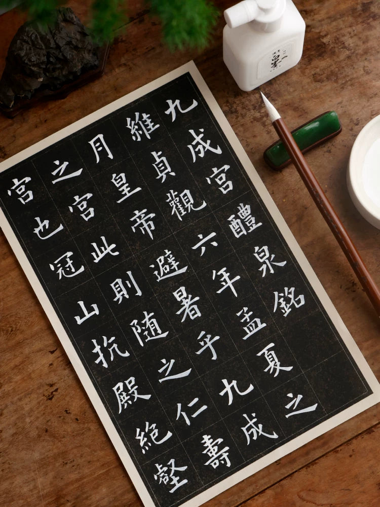White Chinese calligraphy on black gridded paper beside a Hanmo white ink bottle and brush