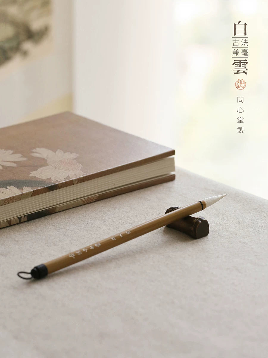 Wen Xin Tang Bai Yun bamboo-handled calligraphy brush with hanging loop on a dark brush rest beside a book
